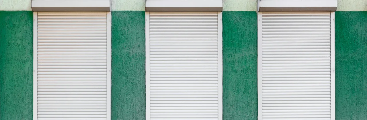 Tres cortinas metálicas blancas cerradas sobre una pared verde